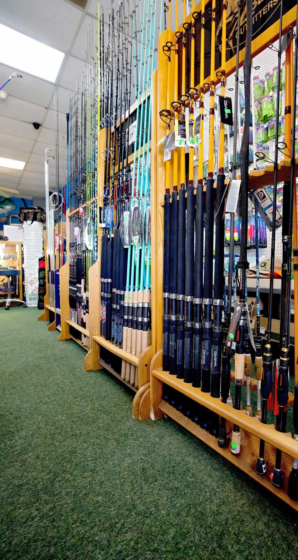 Low angle along wooden floor racks of orange Daiwa boat rods, teal Tail Tamer inshore rods and dark spinning rods