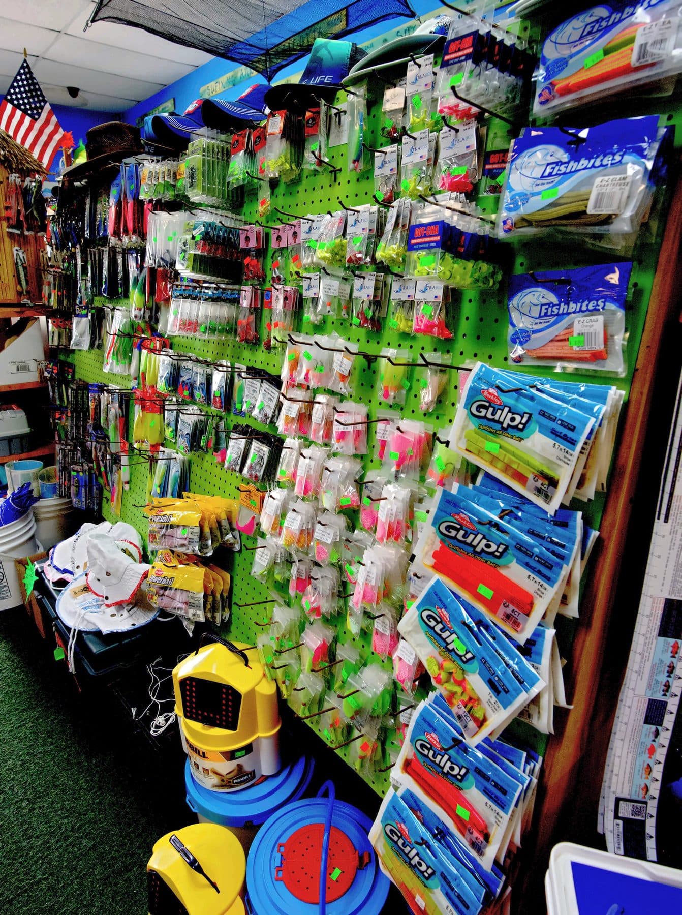 Bright green pegboard of jig heads and pompano jigs with Berkley Gulp! and Fishbites bait strips, bait buckets below