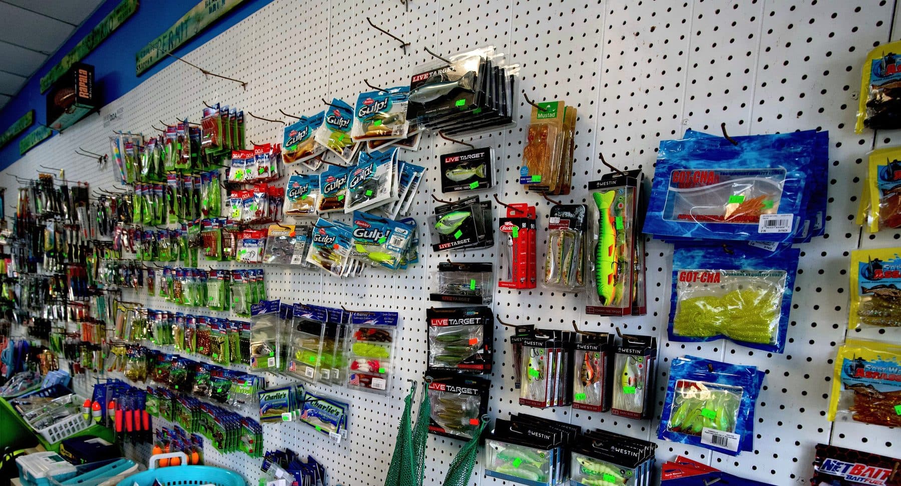 White pegboard wall of Berkley Gulp!, LIVETARGET, Westin, Got-Cha and Salt Water Assassin soft plastics above a counter