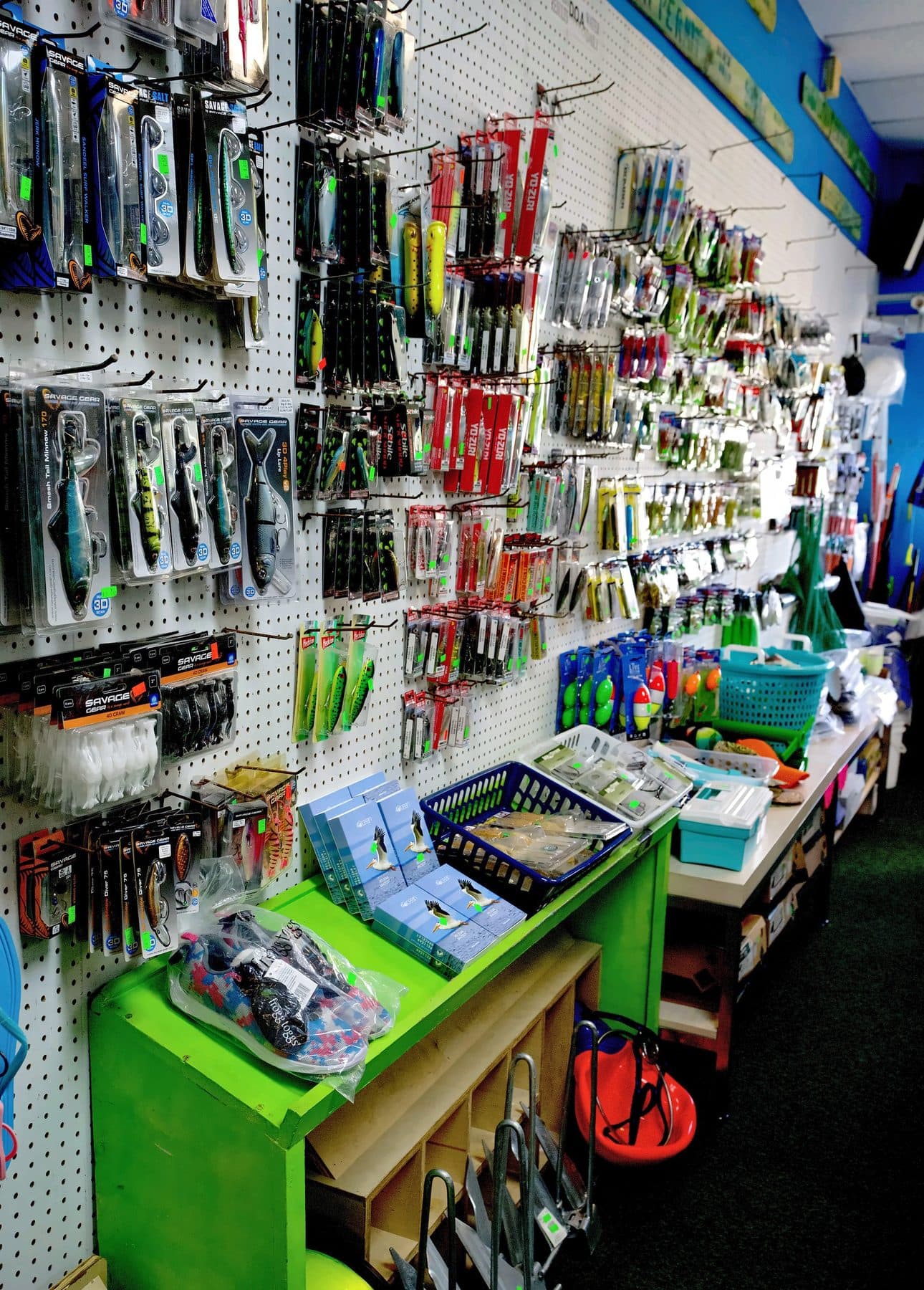 Pegboard wall of Savage Gear swimbaits, Yo-Zuri plugs and Heddon topwaters above a green shelf of boxed bracelets